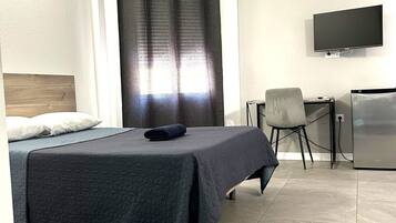 Una habitación de hotel con cama, escritorio, silla, televisor y aire acondicionado.