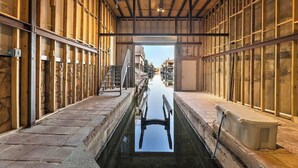 Een smalle gang met een waterkanaal in het midden, houten wanden en uitzicht op de gebouwen daarbuiten.