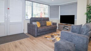 A modern living room with a grey sofa, a TV, and a patterned rug. - Falcon House (Tintagel)