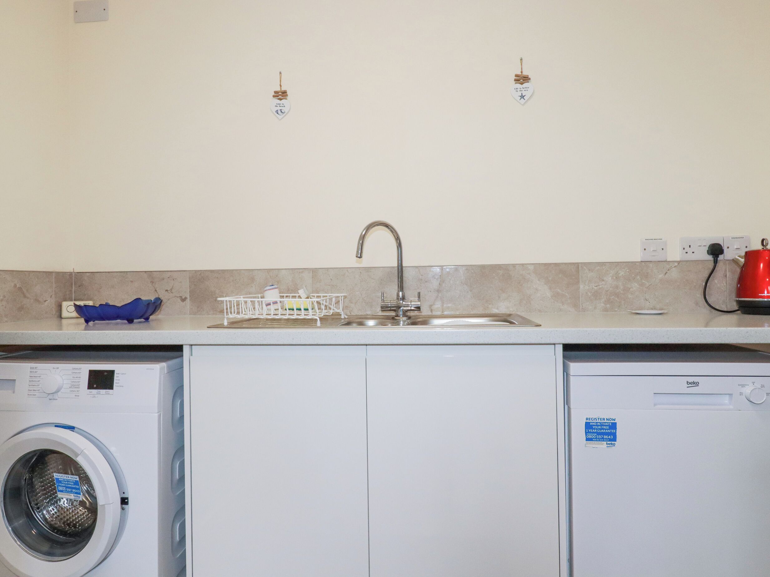 Cocina compacta con lavadora, un lavabo y una tetera roja.