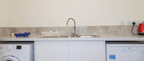 Cocina compacta con lavadora, un lavabo y una tetera roja.
