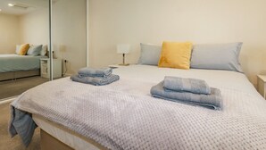 A neatly made bed with a folded towel, a bedside lamp, and a mirror on the wall. - Falcon House (Tintagel)