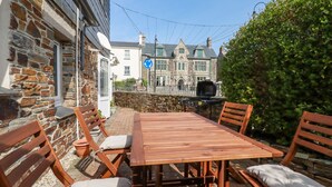 An outdoor patio with a wooden table and chairs, a barbecue grill, and a stone wall. - Falcon House (Tintagel)