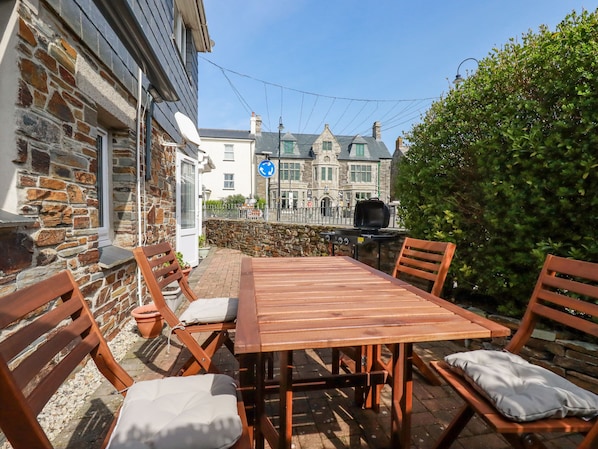 An outdoor patio with a wooden table and chairs, a barbecue grill, and a stone wall. - Falcon House (Tintagel)
