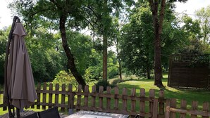 An outdoor patio with a table and chairs, a wooden fence, and a view of a grassy area with trees. - Le Séchoir, Cottage of 75 m2 for 2 people with swimming pool, large park (MONMARVES)