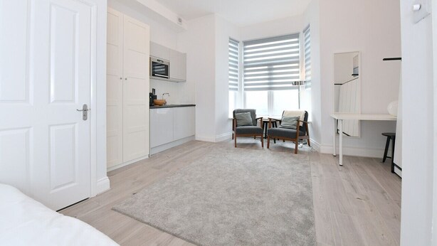 A modern apartment with a kitchen, a dining area with two chairs, a large window with blinds, and a white door. - F69 21 · London Studios Shepherds Bush near Central Line (London)