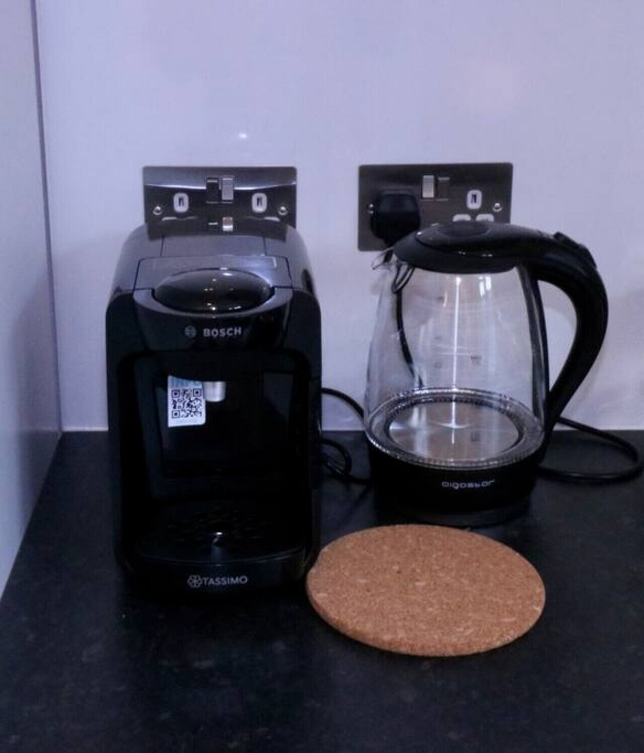 A Bosch Tassimo coffee maker and a glass coffee pot on a black countertop.