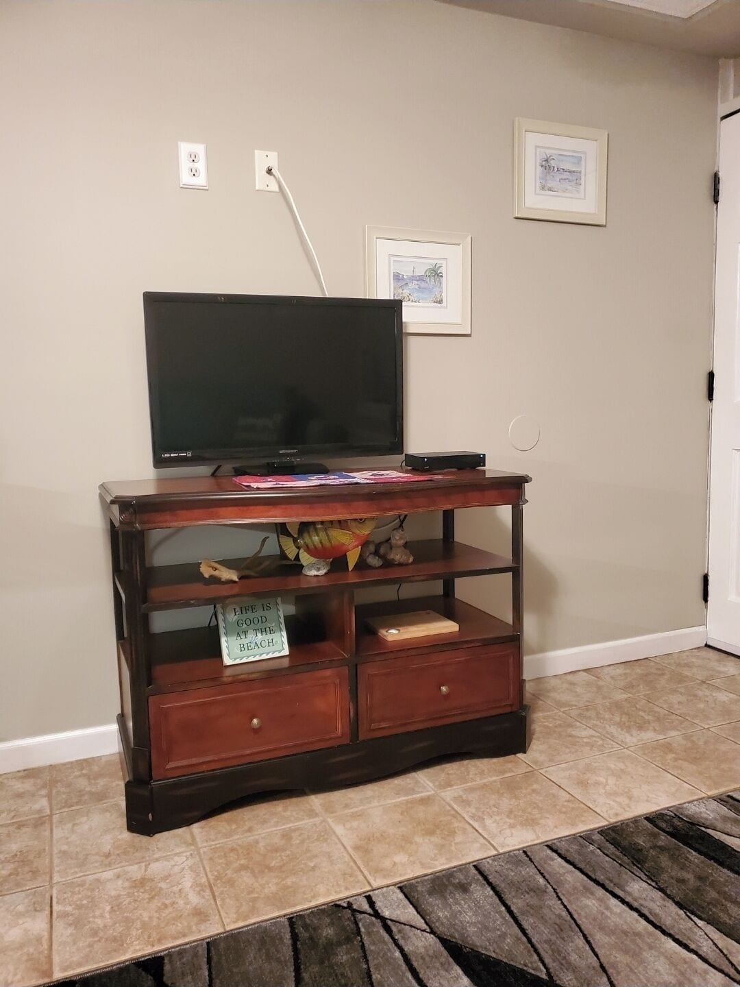 A wooden entertainment center with a flat-screen TV, a fish decoration, and a motivational sign.