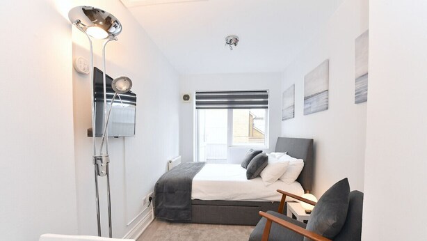 Un dormitorio con una cama, una silla, un escritorio, un televisor y una ventana.