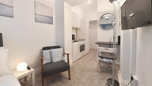 Un espacio habitable moderno y funcional con kitchenette, zona de comedor y de estar, con una silla y una mesita.