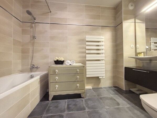 Une salle de bain moderne avec une baignoire, un meuble-lavabo avec un miroir et un porte-serviettes.
