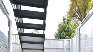 Une terrasse avec une table et des chaises, un mur en briques et une clôture blanche.