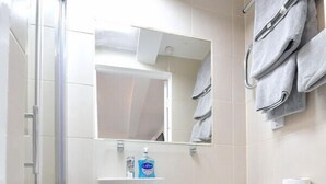 Un bagno moderno con box doccia in vetro, un water bianco, un lavandino con specchio sopra e un cestino.