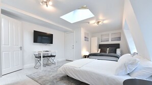 Una camera da letto con un letto, una scrivania, una sedia, una televisione a schermo piatto e un lucernario.