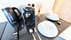 Una encimera de cocina con una cafetera, un hervidor y un control remoto.