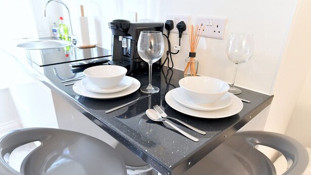 Una cocina moderna con encimera negra, dos tazones blancos, una copa de vino y una cafetera.