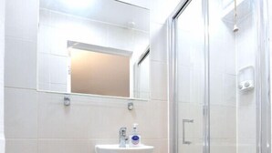 Un baño con inodoro, lavamanos, espejo y ducha con mampara de vidrio.