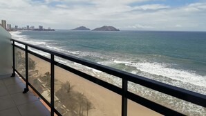 A balcony with a view of the ocean, beach, and distant cityscape. - Condos Perla (Mazatlán)