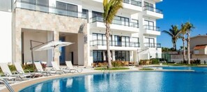 A modern hotel with a swimming pool, sun loungers, and palm trees. - Condos Perla (Mazatlán)