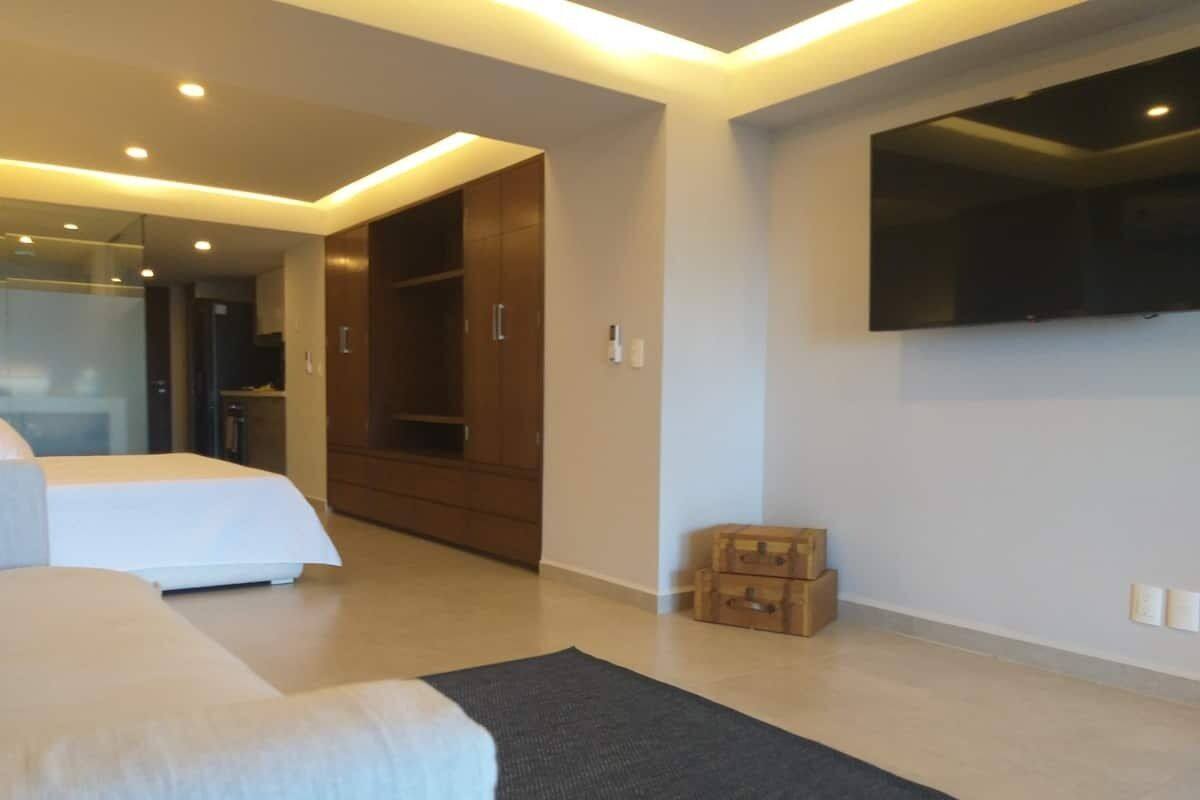 A modern hotel room with a large bed, a flat-screen TV mounted on the wall, and a walk-in closet.