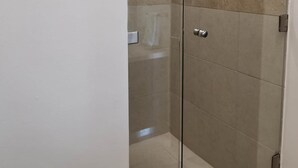 A glass-enclosed shower stall with a handheld showerhead, tiled walls, and a visible drain. - Condos Perla (Mazatlán)