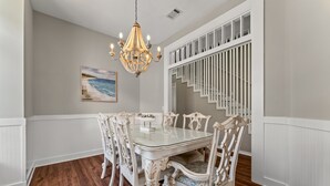 A dining area with a white table and chairs, a chandelier, and a staircase with white railings. - Sleeps 16 / Walk to Beach / 6BR w/ Bunk Room / Perfect for Families & Groups (Destin)