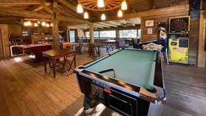 A pool table in a wooden-floored room with a bar area and dartboards. - Mas Fuselles  (Cornella del Terri)