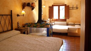 A cozy bedroom with a large bed, a small table, a chair, a fireplace, and a window with wooden shutters. - Mas Fuselles  (Cornella del Terri)