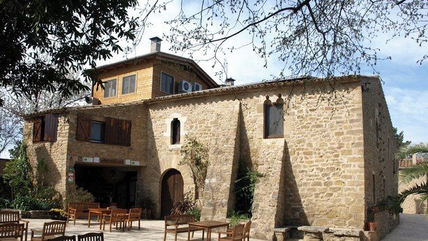 A stone building with a wooden balcony and outdoor seating area. - Mas Fuselles  (Cornella del Terri)