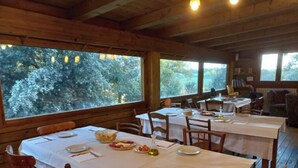 A dining area with tables set for two, wooden walls, and large windows offering a view of trees. - Mas Fuselles  (Cornella del Terri)