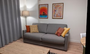 A grey sofa with patterned cushions, a floor lamp, and two framed artworks on the wall.