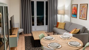 Una sala de estar moderna con comedor, cortinas grises, un sofá gris y un televisor sobre un mueble.