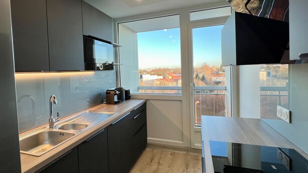 Una cocina moderna con un amplio ventanal, muebles oscuros y un lavamanos de acero inoxidable.