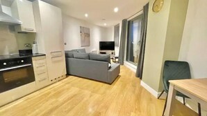 Eine moderne Wohnung mit einer Küche, einem grauen Sofa, einem Esstisch und einem Fernseher im Wohnbereich.