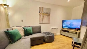 Ein modernes Wohnzimmer mit einem grauen Ecksofa, einem Sitzsack, einem Flachbildfernseher und minimalistischer Einrichtung.