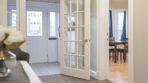 A room with a white door, a dining table with chairs, and a vase with flowers on a table. - Riverside Inn (New Glasgow)
