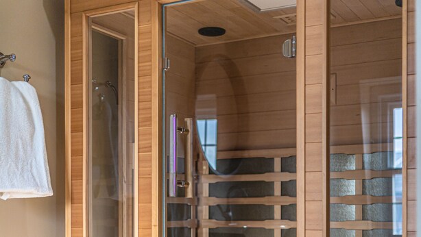 A wooden sauna with glass doors, a wooden bench, and a towel rack. - Riverside Inn (New Glasgow)