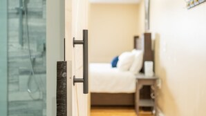 A hotel room with a glass shower enclosure, a bed with white bedding, and a small bedside table. - Riverside Inn (New Glasgow)