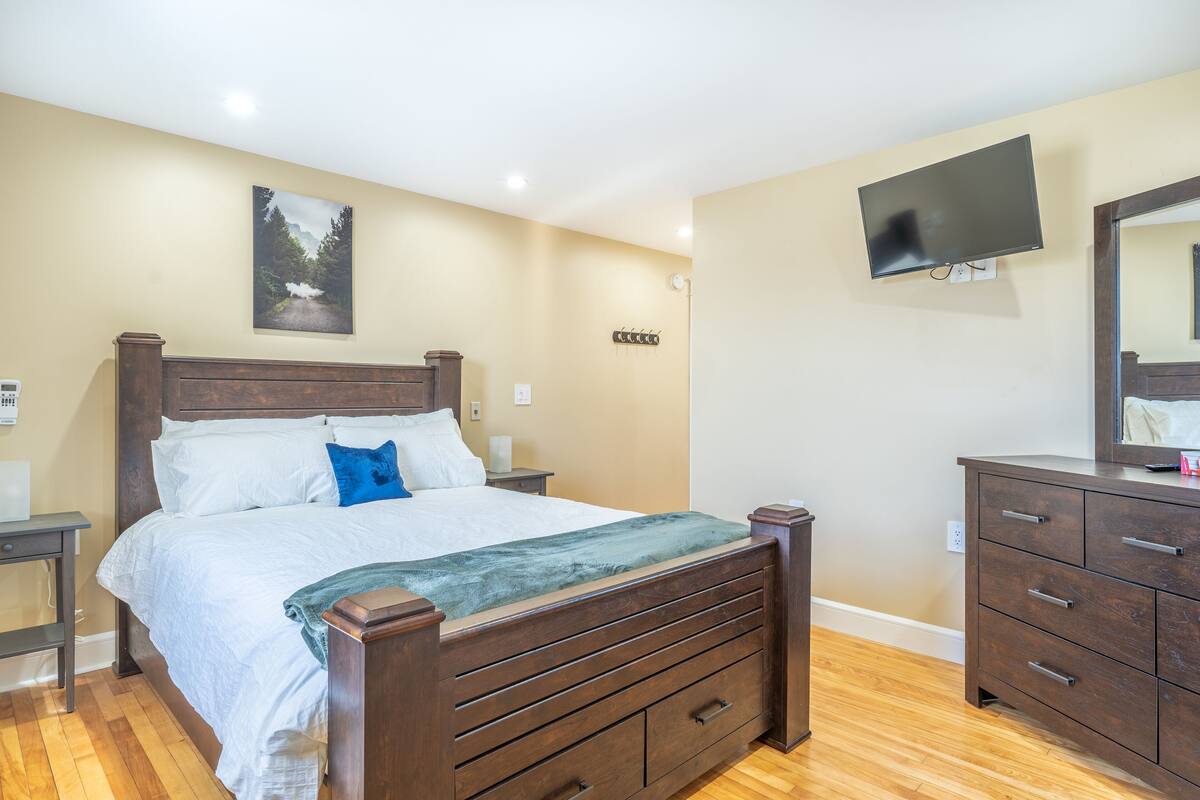 Un dormitorio con cama de madera, mesita de noche, cómoda, televisor de pantalla plana y un cuadro en la pared.