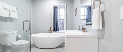 A modern bathroom with a glass shower enclosure, a freestanding bathtub, a toilet, and a sink with a mirror.
