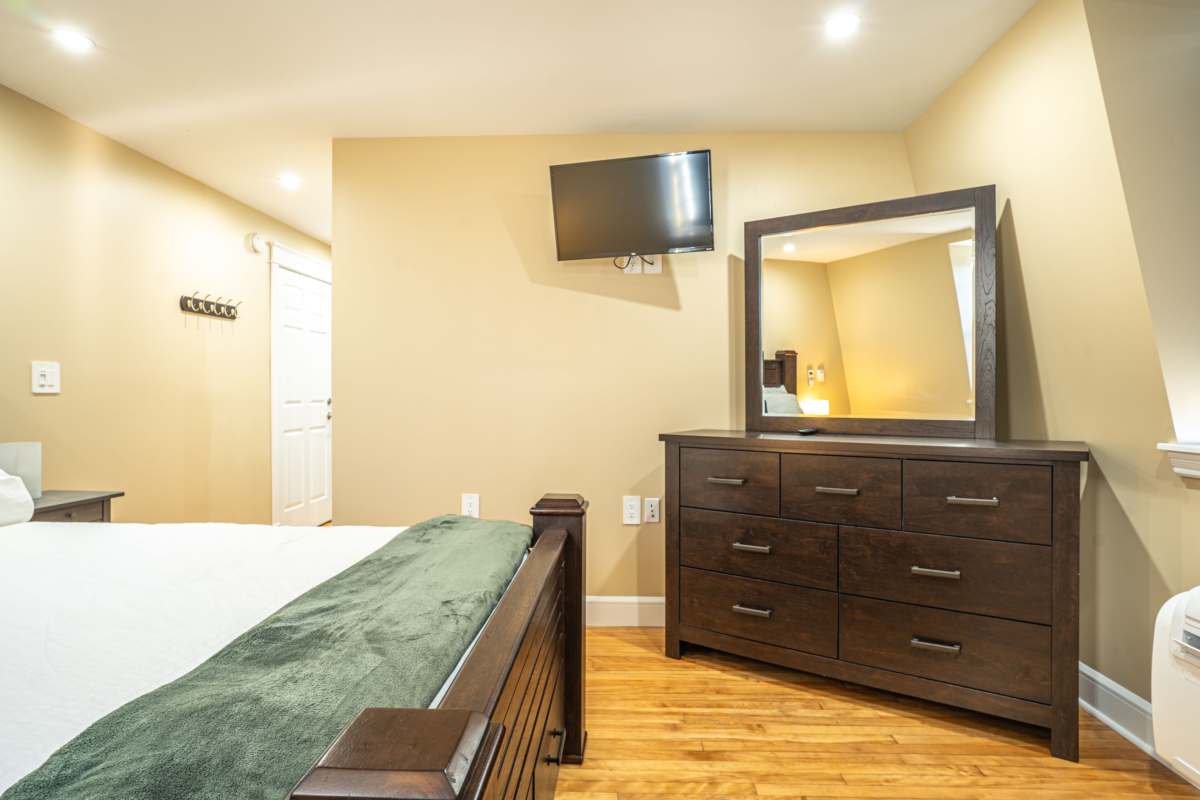 A bedroom with a bed, dresser, TV, and mirror.