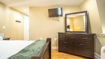 A bedroom with a bed, dresser, TV, and mirror.