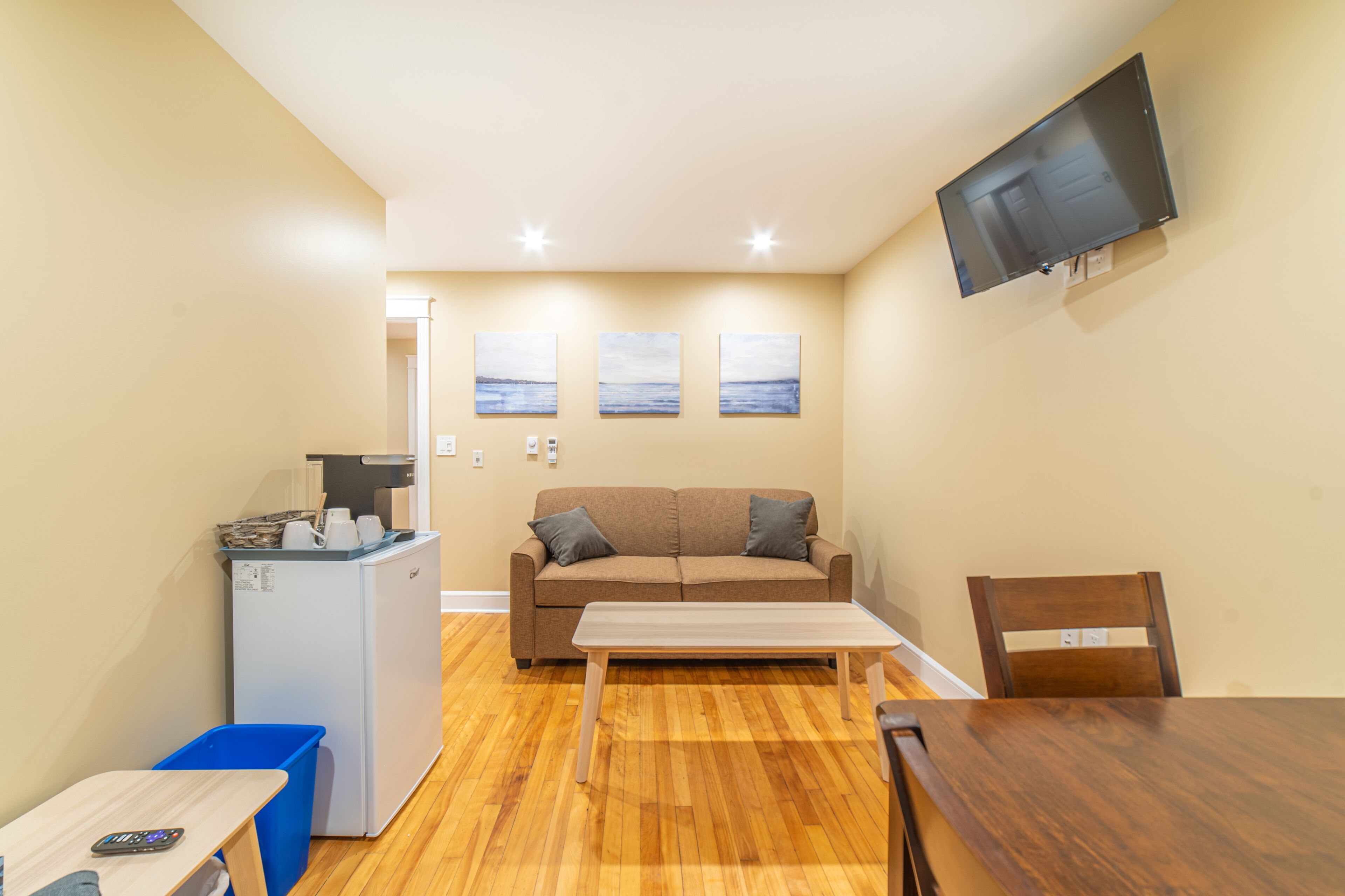Un espacio habitable compacto con kitchenette, un sofá, una mesa de comedor y un televisor montado en la pared.