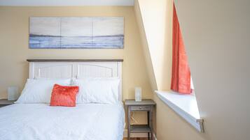Un dormitorio con cama, una mesita de noche, una ventana con cortinas y un cuadro en la pared.