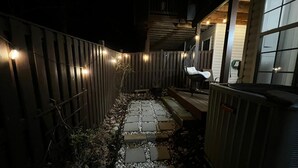 A narrow pathway with stepping stones leading to a wooden deck, surrounded by a wooden fence with string lights. - Woodland Park Studio (Herndon)