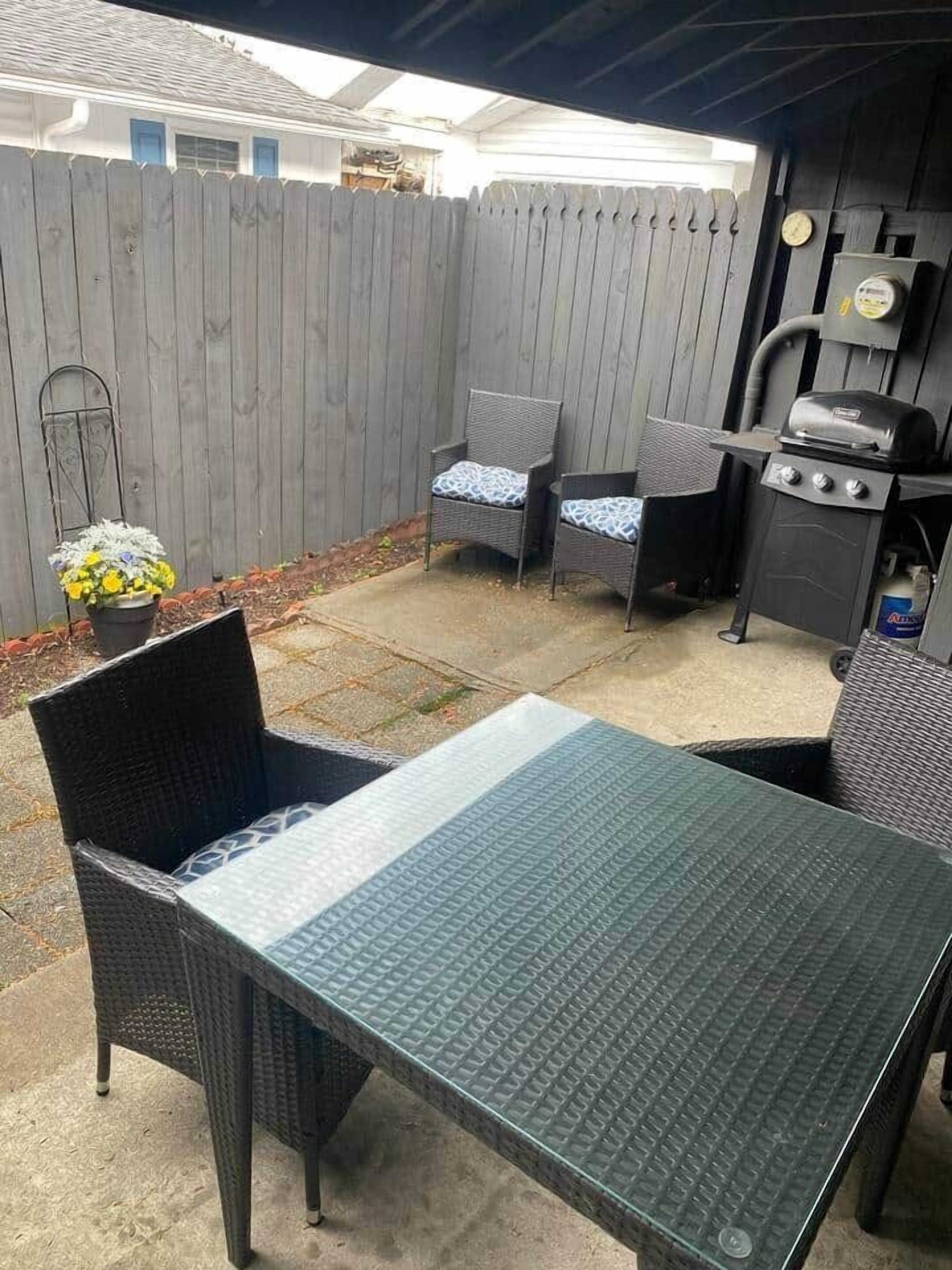 A patio with a table and chairs, a grill, and a wooden fence.