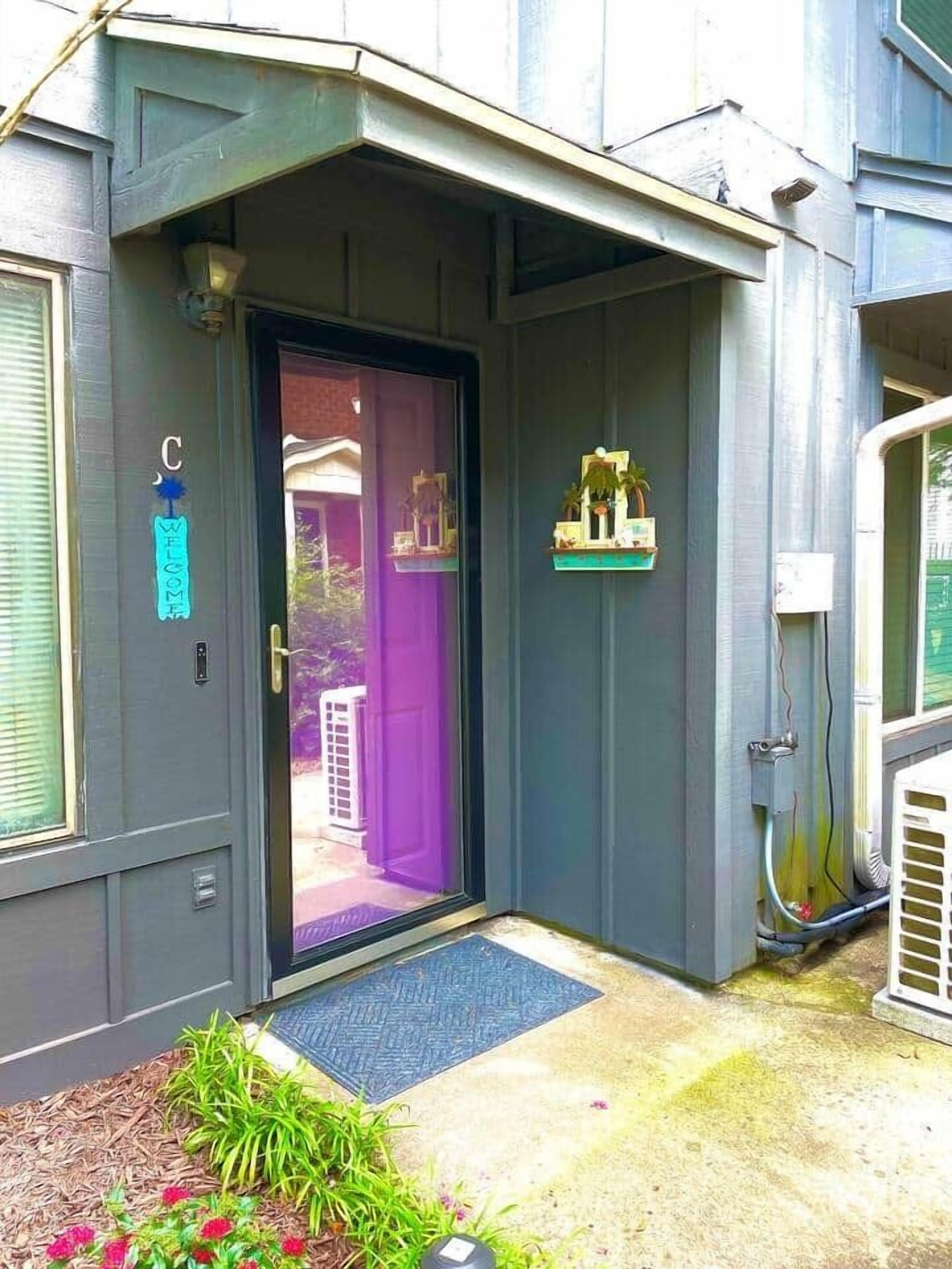 Une maison à l’extérieur d’un gris foncé, avec une porte violette et une pancarte indiquant « Bienvenue ».