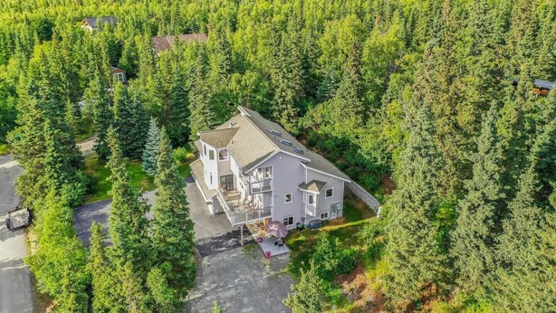 A two-story house surrounded by dense forest, with a driveway leading to the entrance. - Wind Song Retreat on the Anchorage Hillside! (Anchorage)