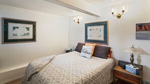 A neatly arranged bedroom with a bed, two wall-mounted lamps, framed artwork, and a bedside table with a lamp and tissues. - Wind Song Retreat on the Anchorage Hillside! (Anchorage)