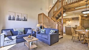 Un vaste salon avec un grand canapé bleu, un escalier en bois et un coin cuisine visible au fond.